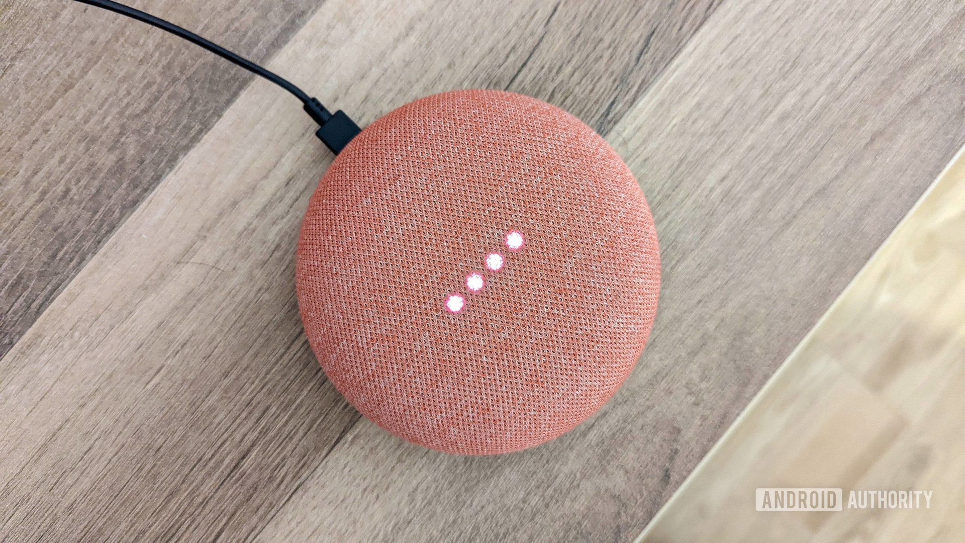 Google Home Mini in coral with lights on, on wooden background